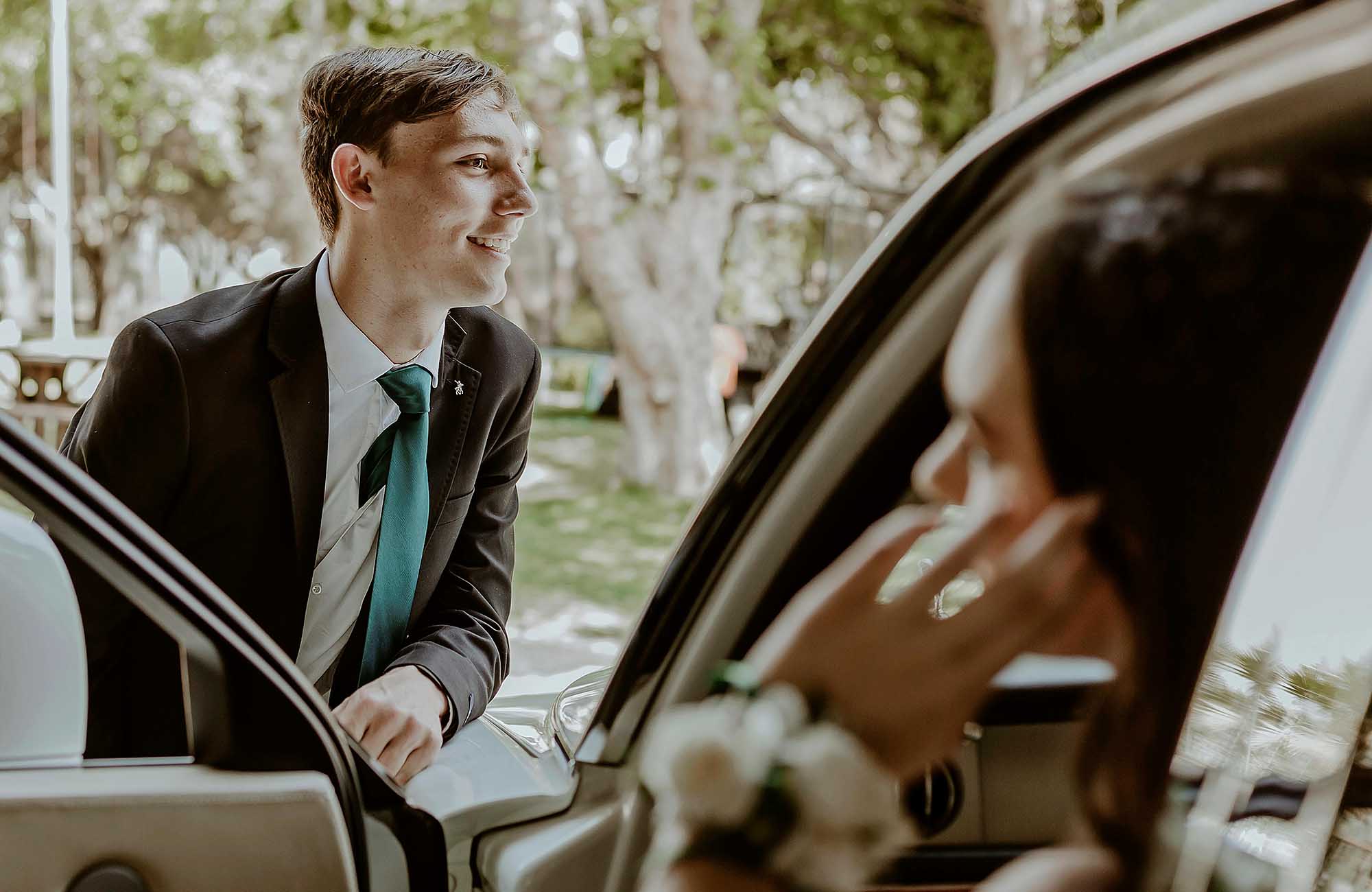 Couple next to car getting ready to go to a school formal wth the girl wearing a corsage