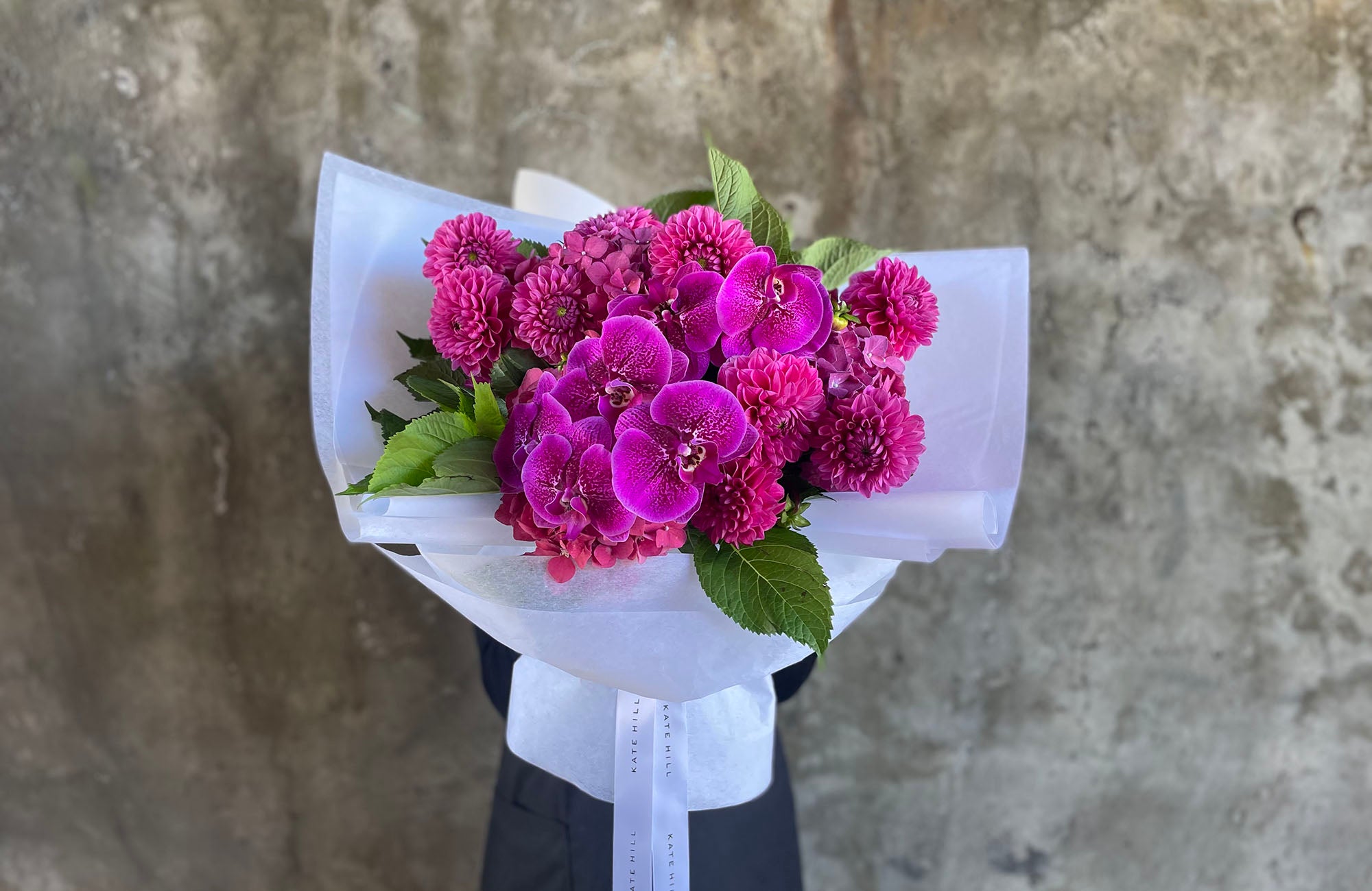 Pink January Birthday Flowers being held by lady with wall behind