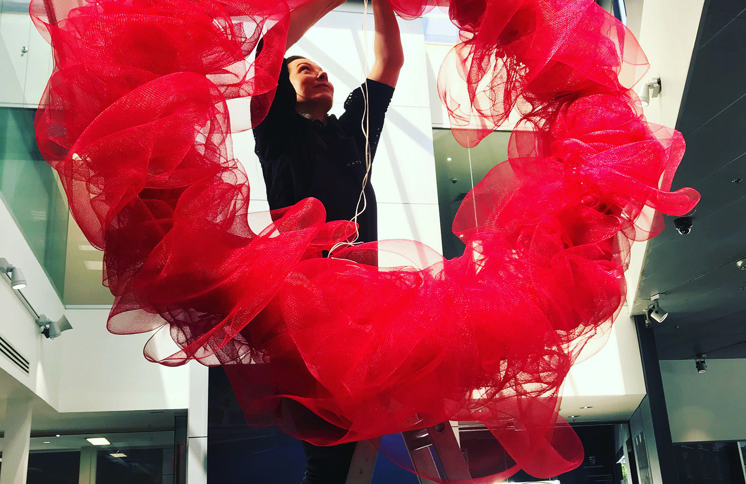 Red modern Christmas wreath being installed in showroom by Kate Hill Flowers