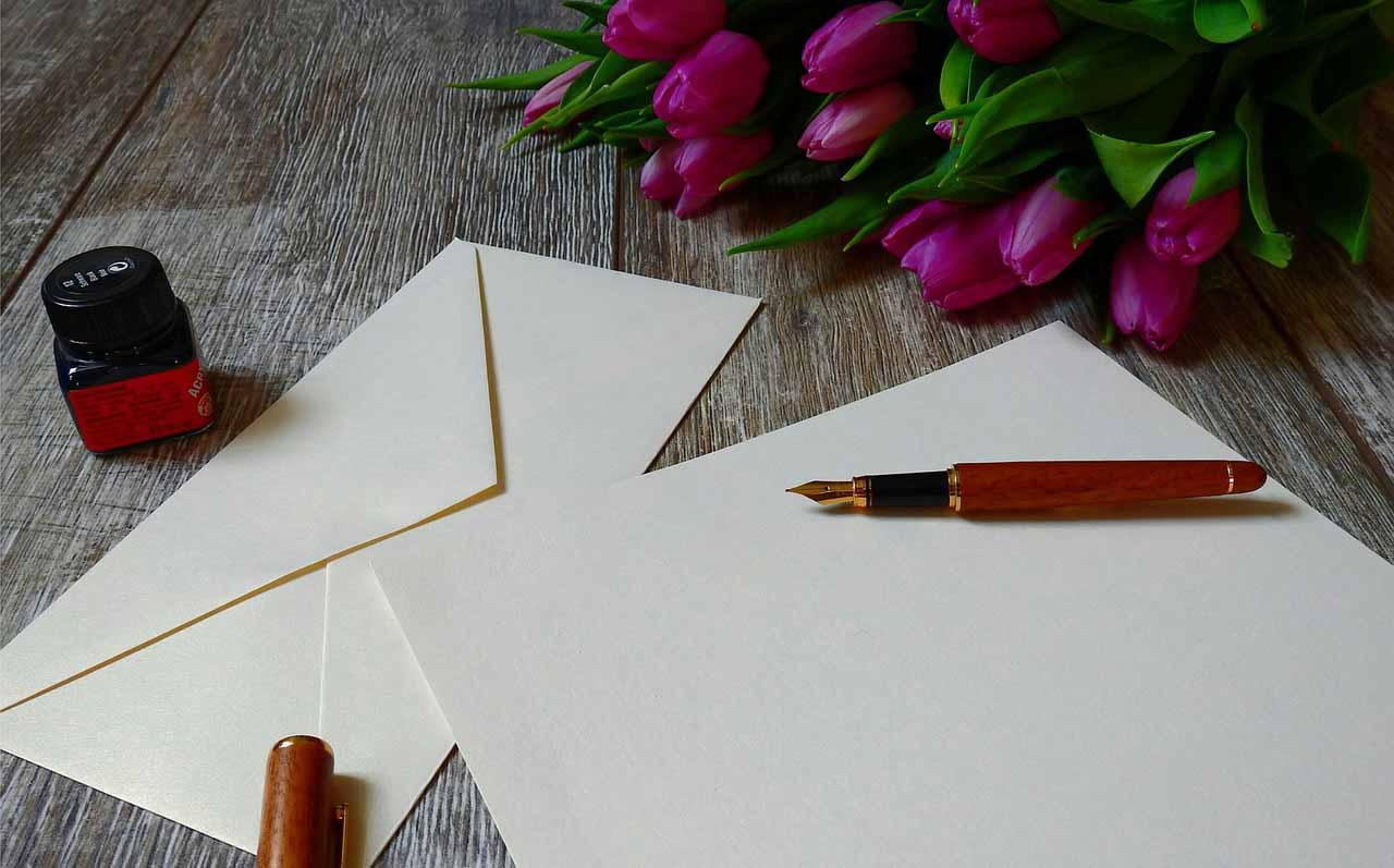 An envelope and card with a pen and flowers placed on a table with no writing