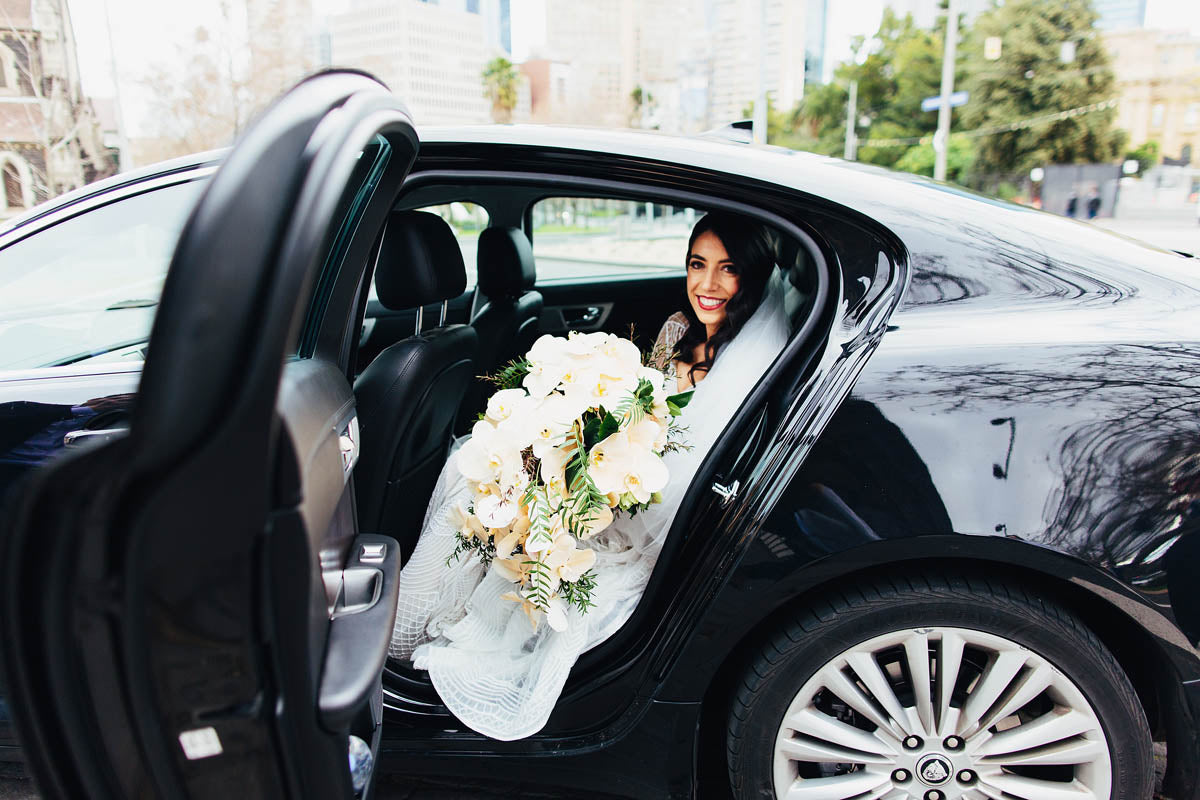Bride exiting car with wedding flowers
