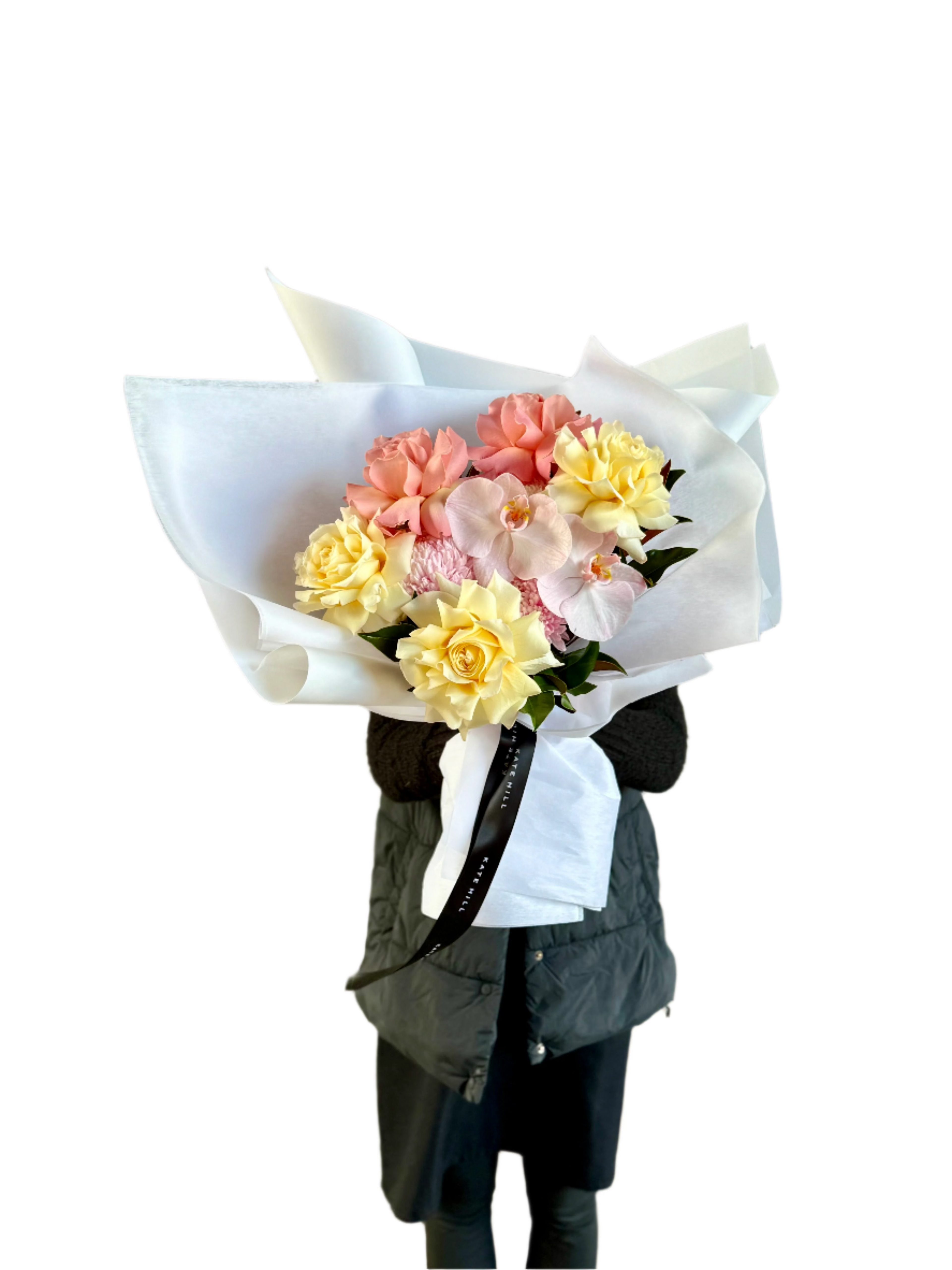 Florist wearing black clothing holding A medium sized lemon and blush gift bouquet in kate hill flower bag, sitting on a black bentwood chair in front of a white wall.
