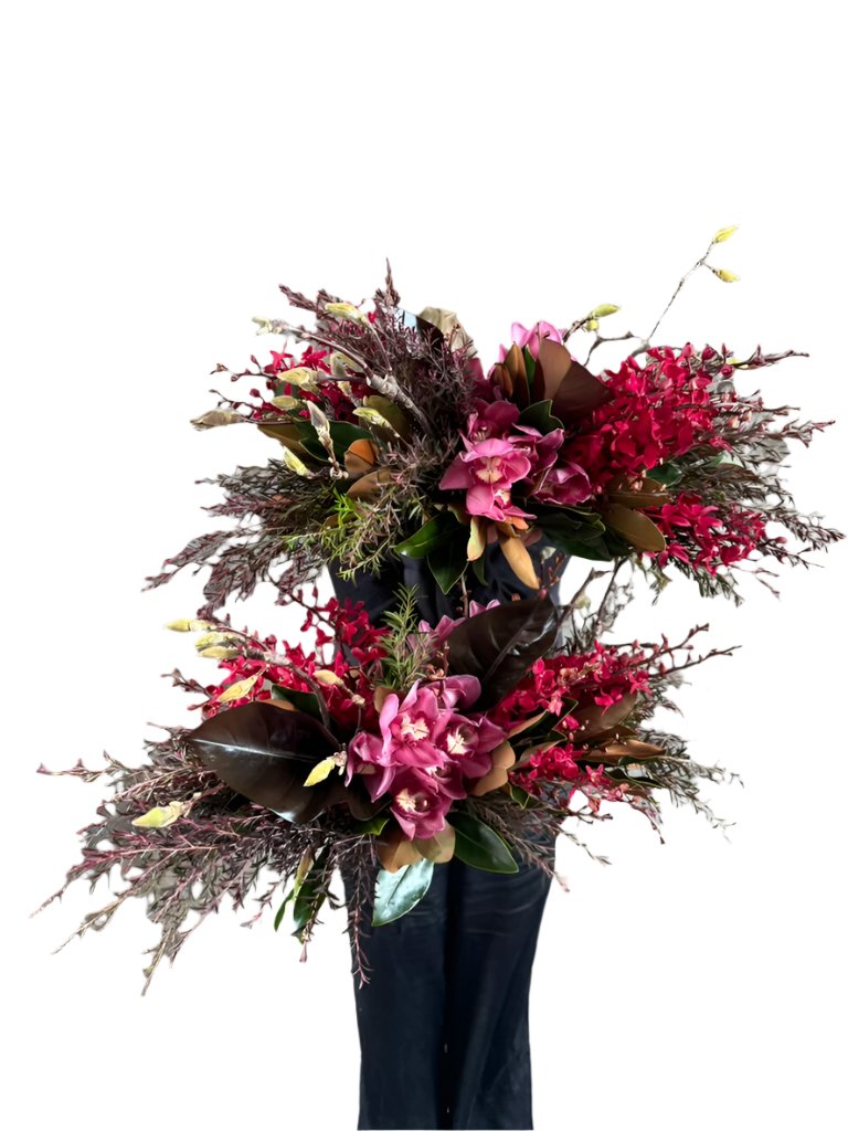 Florist holding 3 GARNET rich red tablescapes, against a concrete wall.