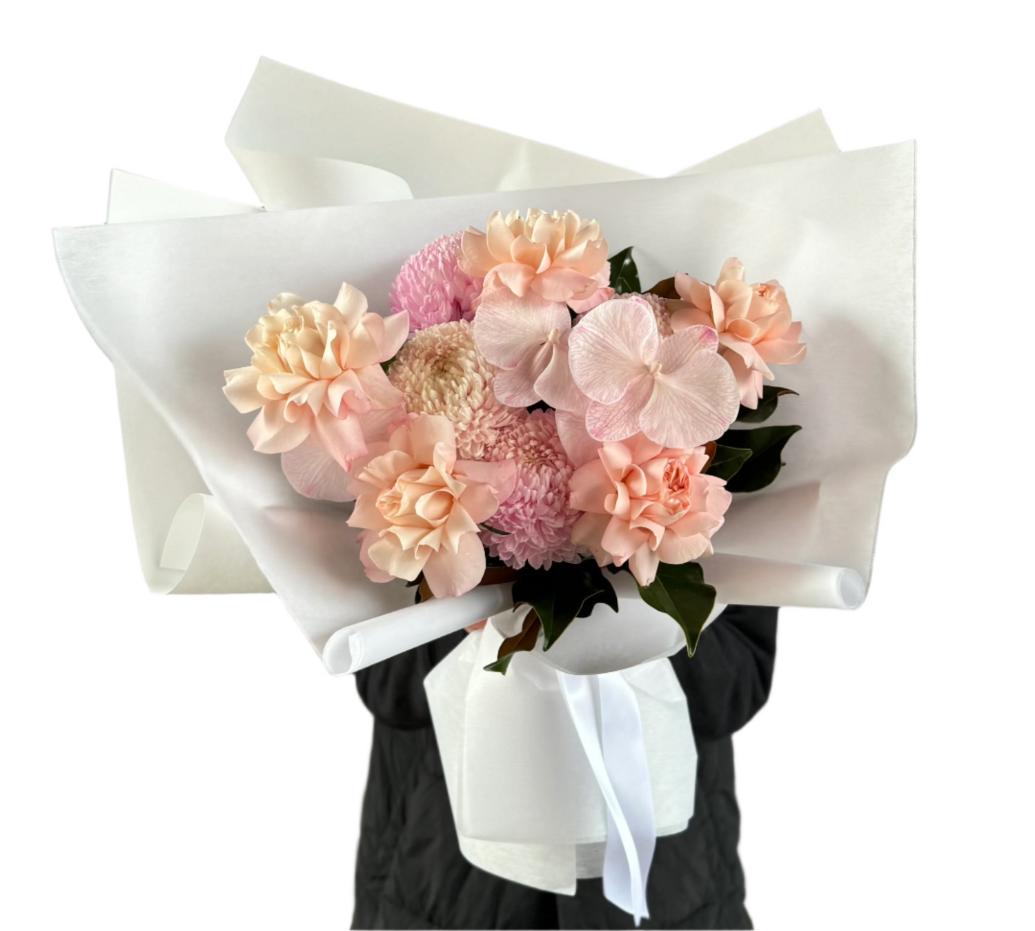 A close up of a blush pink flower bouquet, beautifully wrapped in white signature paper. Florist holding the bouquet in front of a white wall.