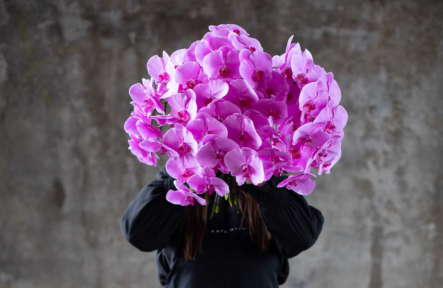 Person holding a large bouquet of pink flowers for flower delivery to Albert Park against a textured wall.