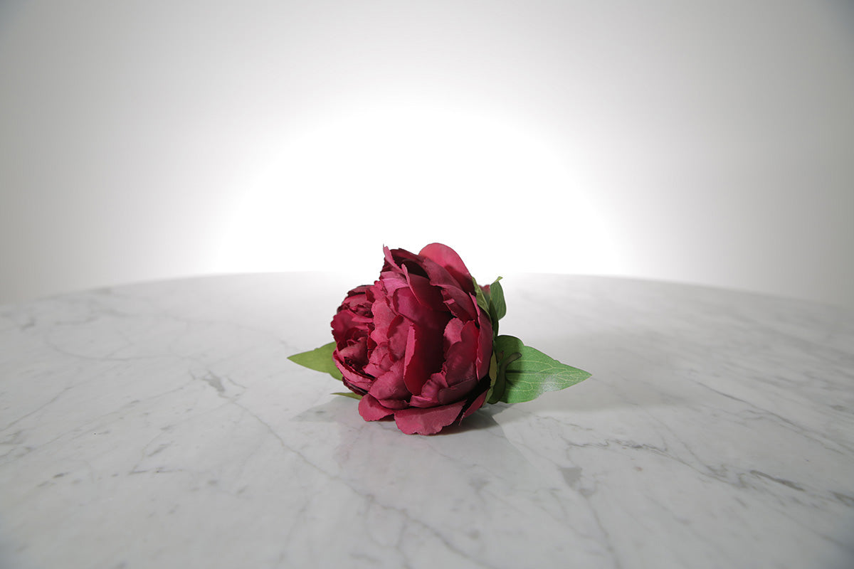 Kate Hill Flowers – artificial burgundy peony rose buttonhole flower with green leaf backing and pearl pin on marble table setting.