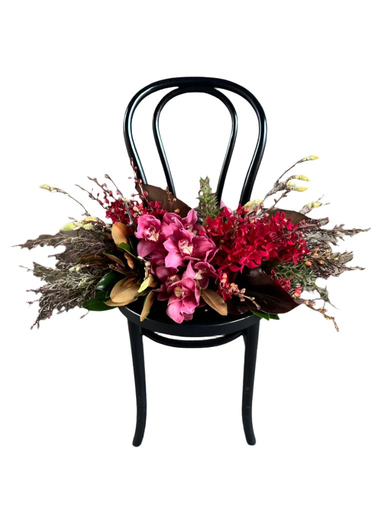 A black bentwood chair with the GARNET rich red tablescape sitting on chair, against a white wall.