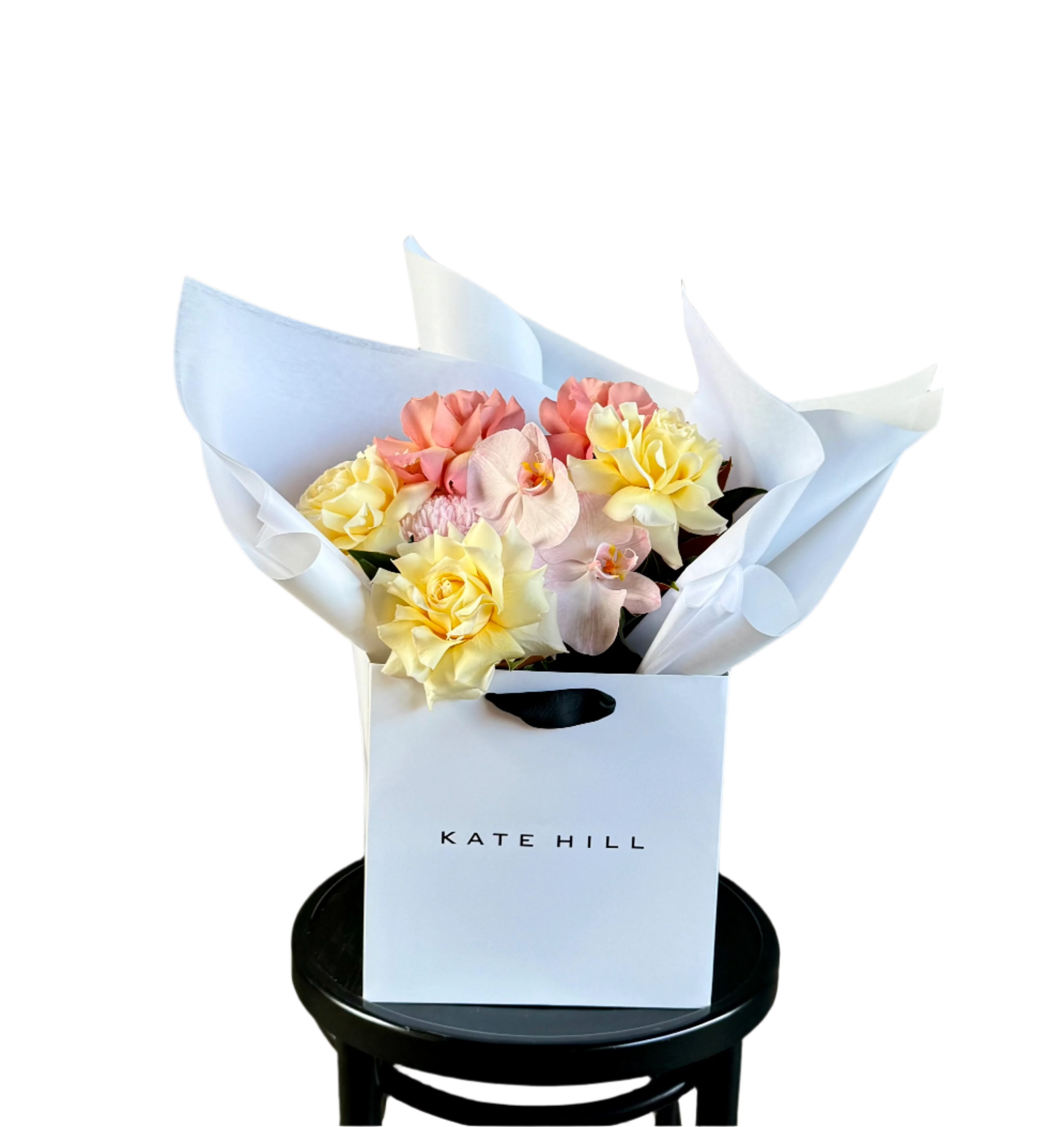 Close up image of A medium sized lemon and blush gift bouquet in kate hill flower bag, sitting on a black bentwood chair in front of a white wall.
