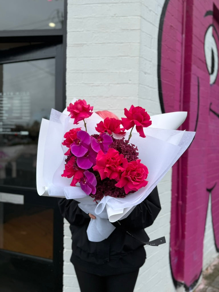Melbourne florist holding a bouquet of pink and red flowers in front of a building with pink artwork.