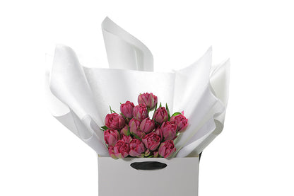A wrapped bouquet of 20 stems of dark double pink tulips. FRANKIE double Tulip bouquet is beautifully gift wrapped in Kate Hill Flowers signature style that includes layers of premium white and silk paper, finished with Kate Hill signature ribbon. Bouquet is placed into our Kate Hill flower bag. Bouquet bag is sitting on a black bentwood chair. Up close image of the FRANKIE double pink tulip bouquet.