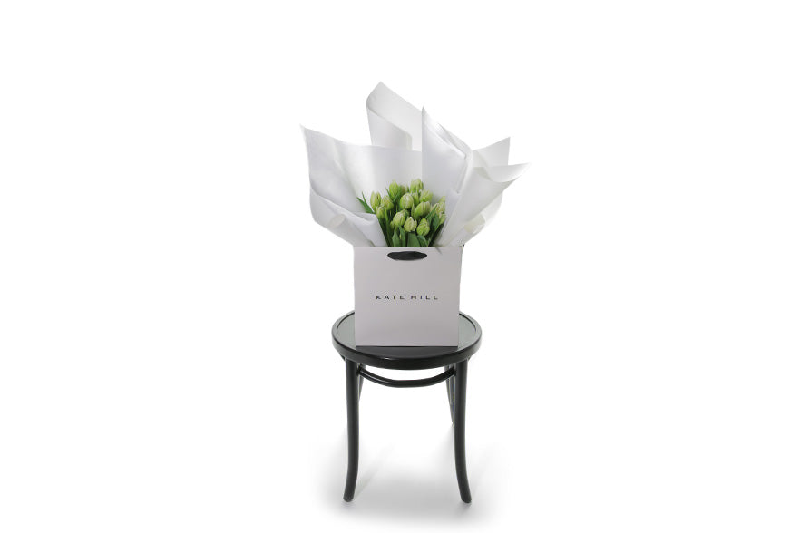 Wide image of white double tulip bouquet. Kate Hill flower bag sitting on a black bentwood chair, displaying fresh premium white double tulip bouquet. Bouquet of 20 stems of white double tulips in image.