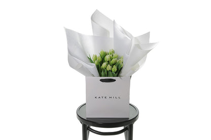 Kate Hill flower bag sitting on a black bentwood chair, displaying fresh premium white double tulip bouquet. Bouquet of 20 stems of white double tulips in image.