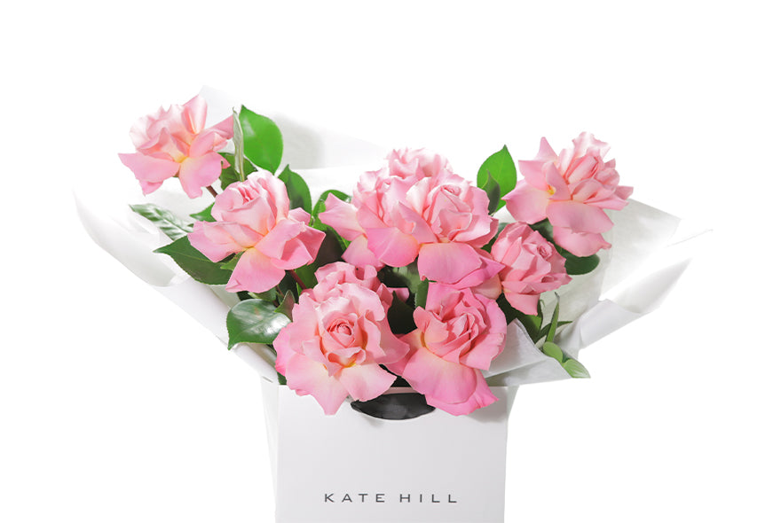 Up close image of the bouquet so you can see the beautiful HERMOSA roses that are reflexed. HERMOSA Rose Bouquet is our best selling watermelon pink rose bouquet, curated with Reflexed watermelon pink roses and green seasonal foliage. Large bouquet of watermelon roses presented in our luxury flower bag so it stays fresh in water. Bouquet bag sitting on a black bentwood chair.