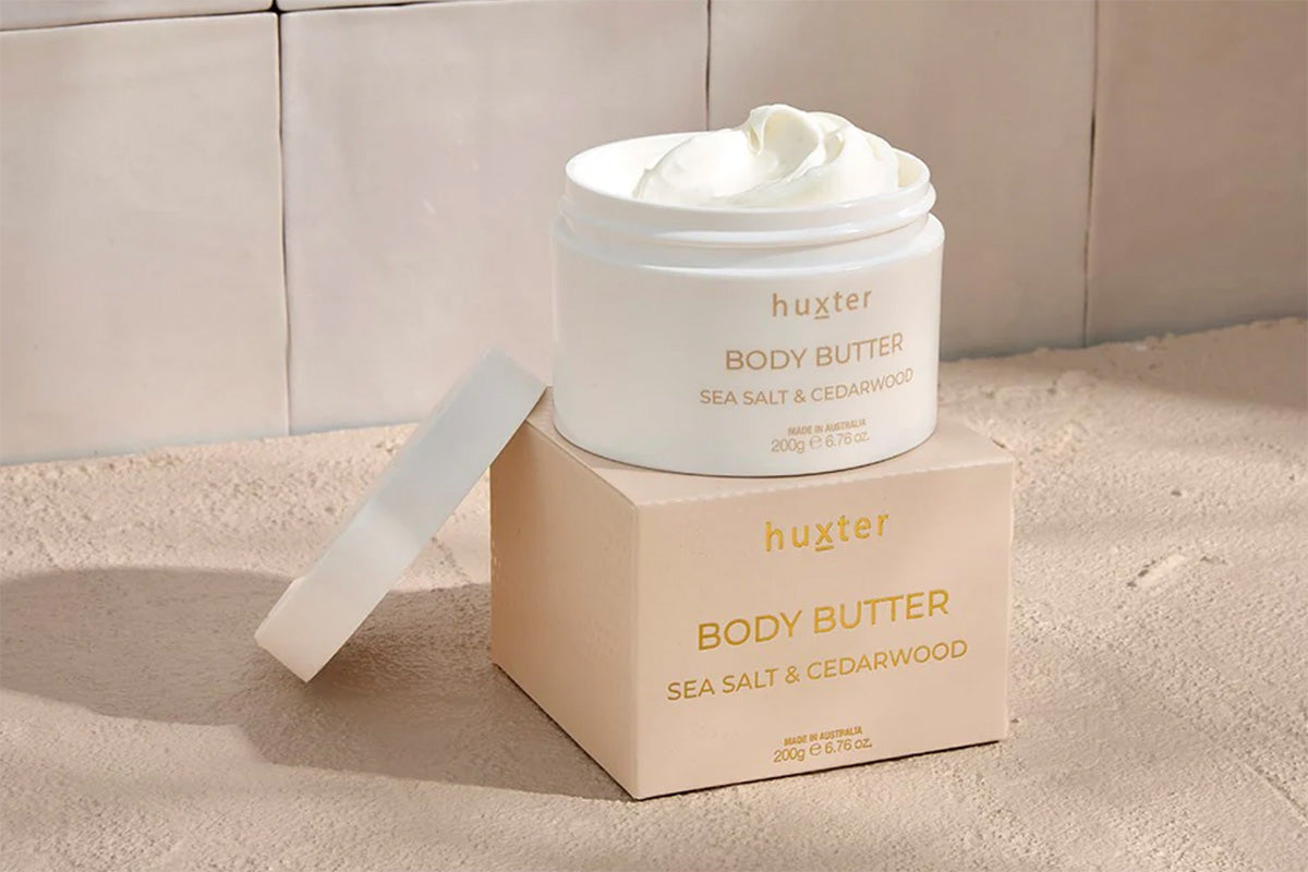 Huxster body butter jar and box on a beige bathroom setting background
