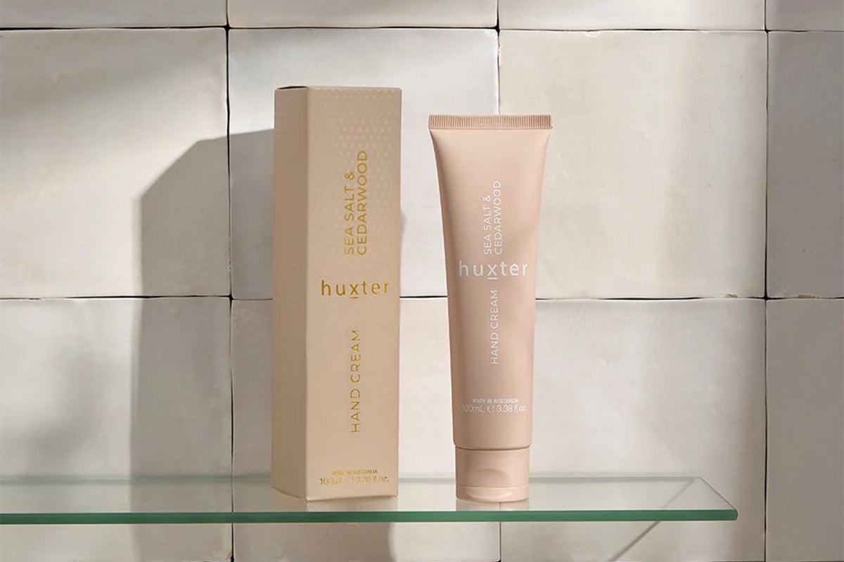 Huxster hand cream and box on a glass shelf with a tiled wall background.