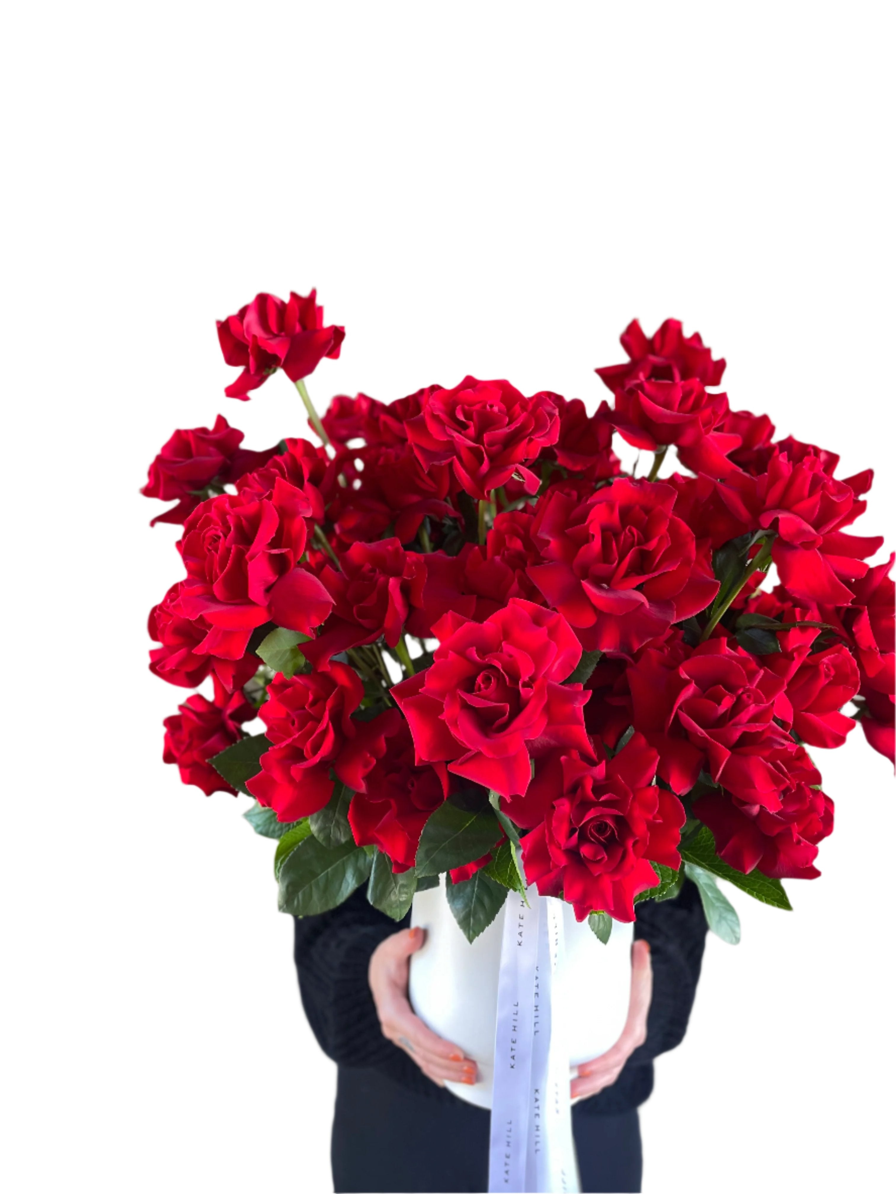 Florist holding A grande design, displaying 50 long stemmed red roses on mass in a large white footed ceramic vase.