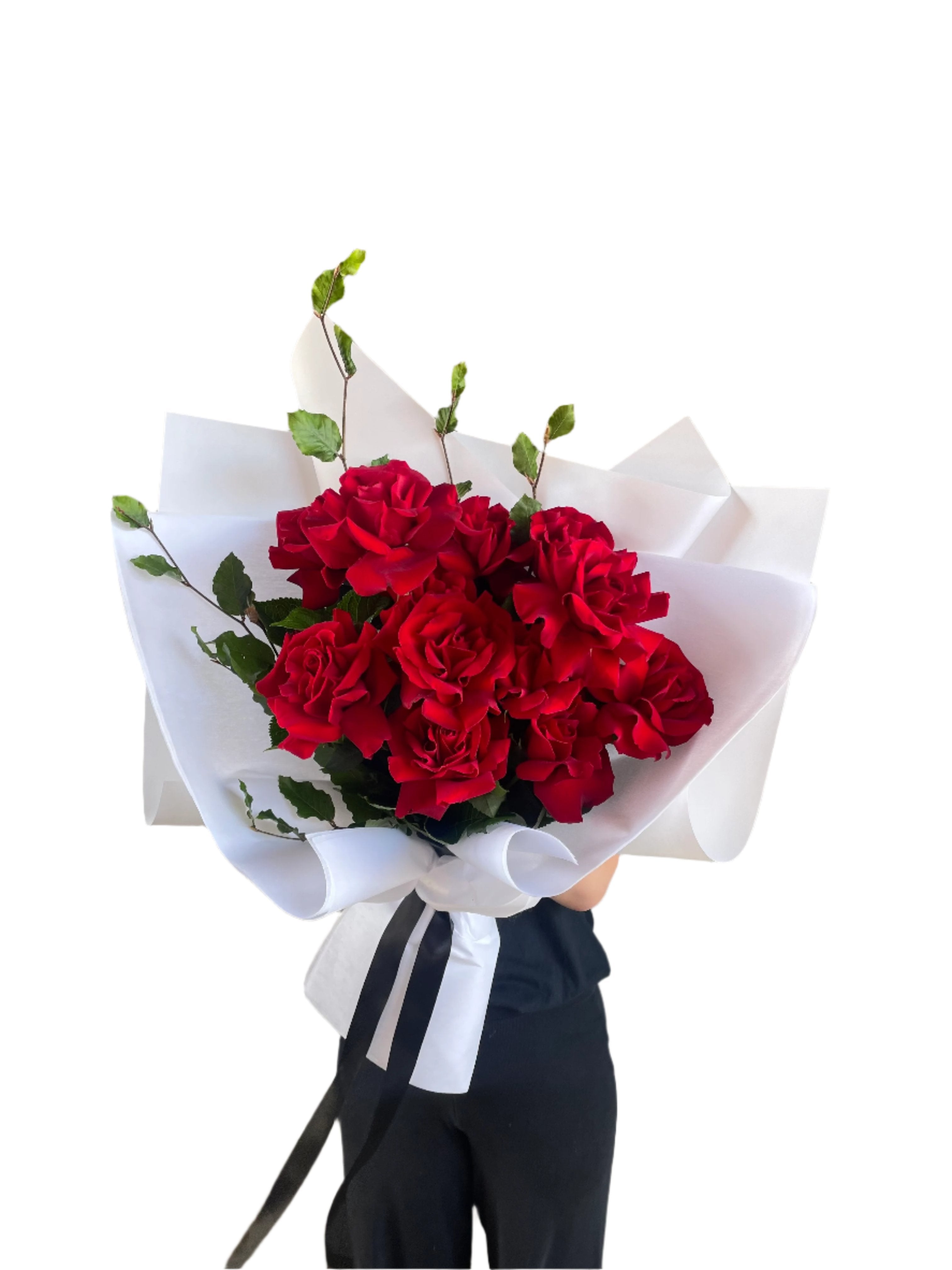 Bouquet of one dozen red roses and foliage. A luxe red rose bouquet designed with 12 premium red roses and foliages, beautifully wrapped with signature KHF wrapping. Florist holding the bouquet in front of a white wall.