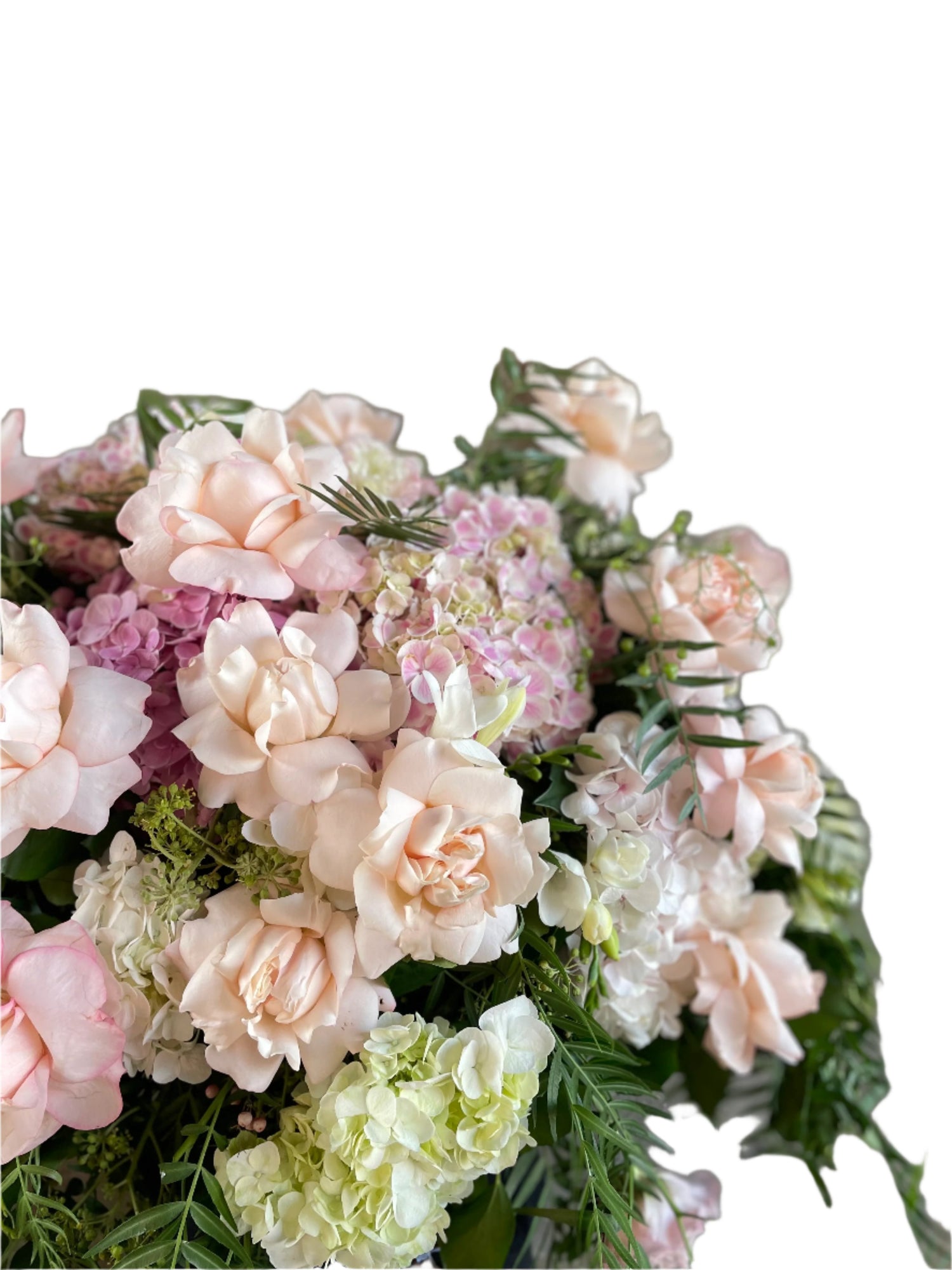 Classic blush roses, blush hydrangeas, lilac stock and foliages feature in a Pastel pink, white and green casket design, held by a florist wearing back, up against a white wall.