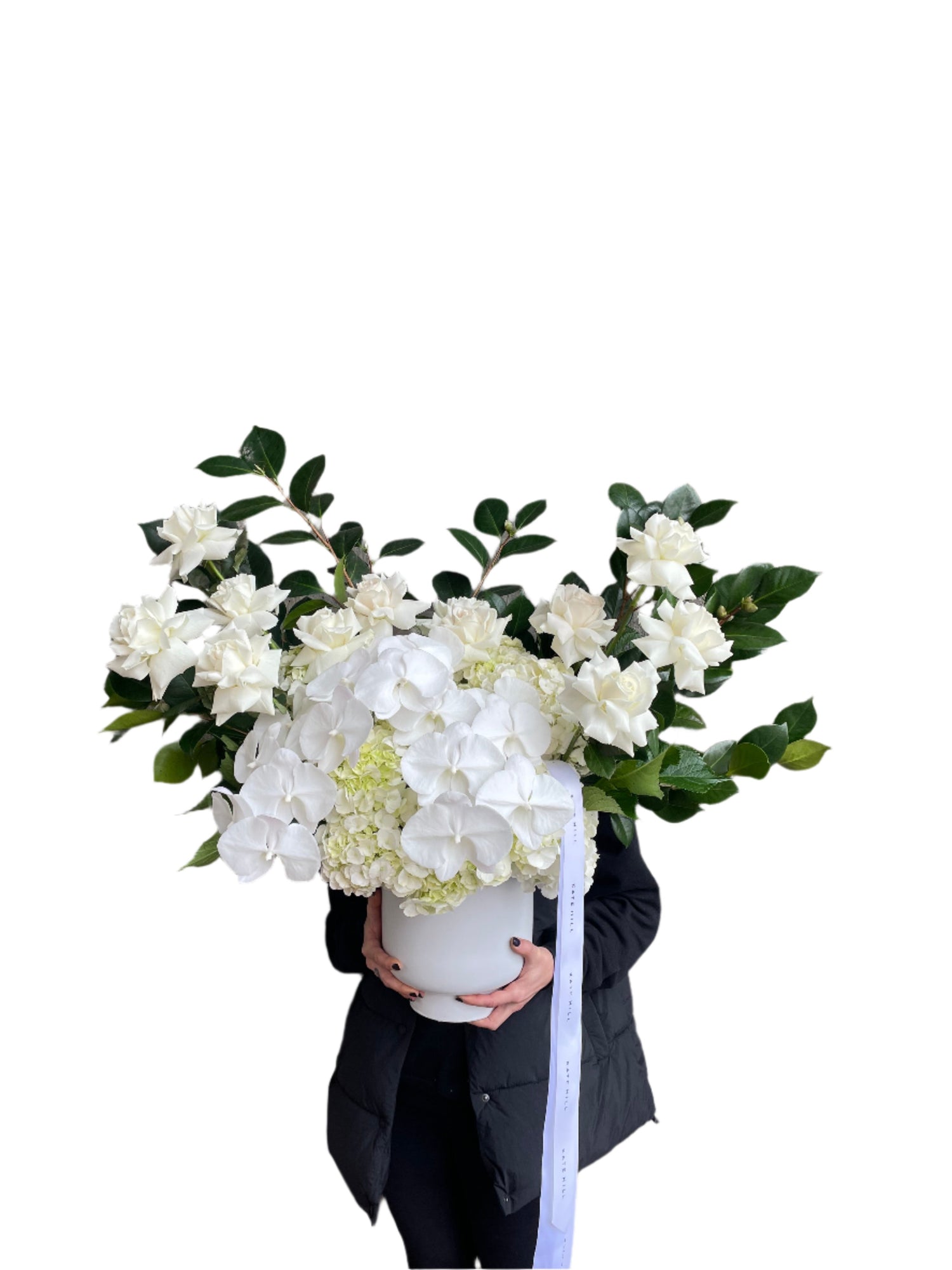 A florist holding the large luxe white flower design sitting on a black bentwood chair with white wall behind.