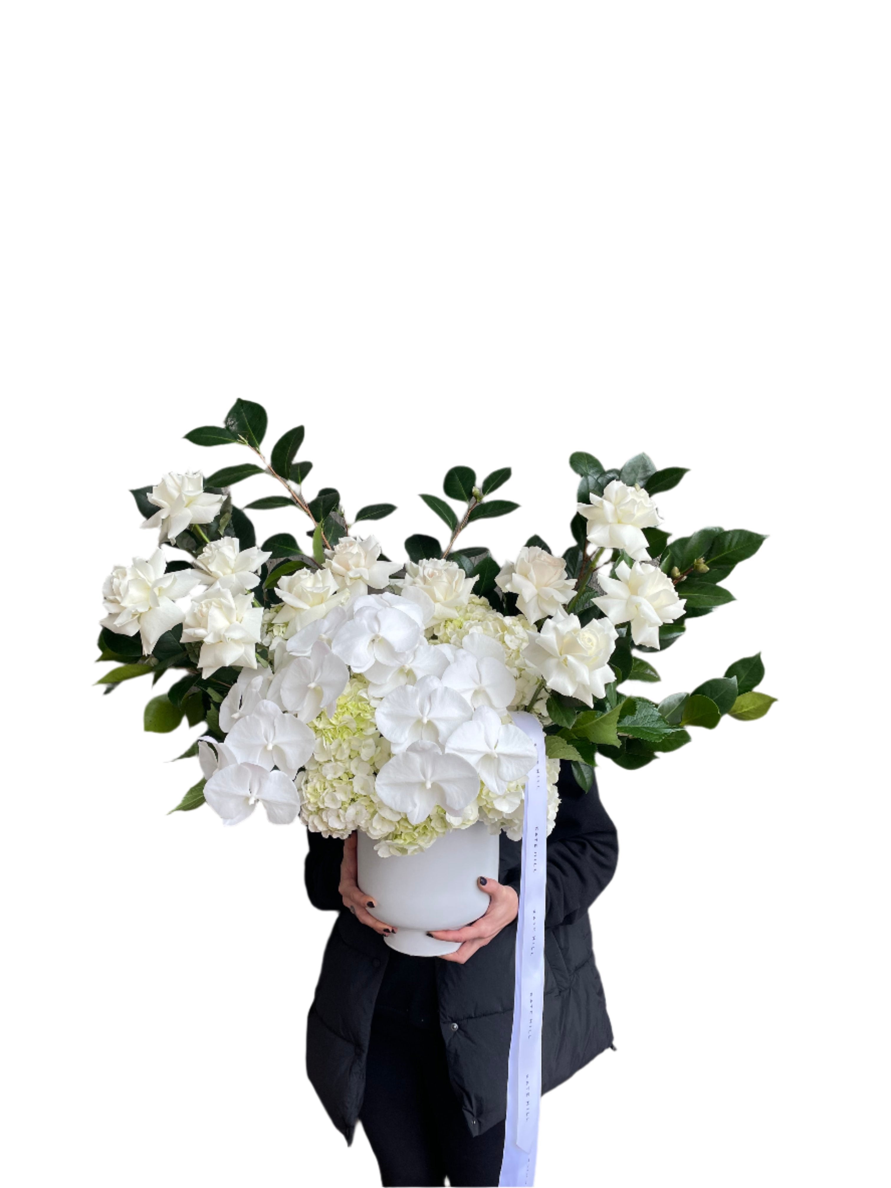 A florist holding the large luxe white flower design sitting on a black bentwood chair with white wall behind.