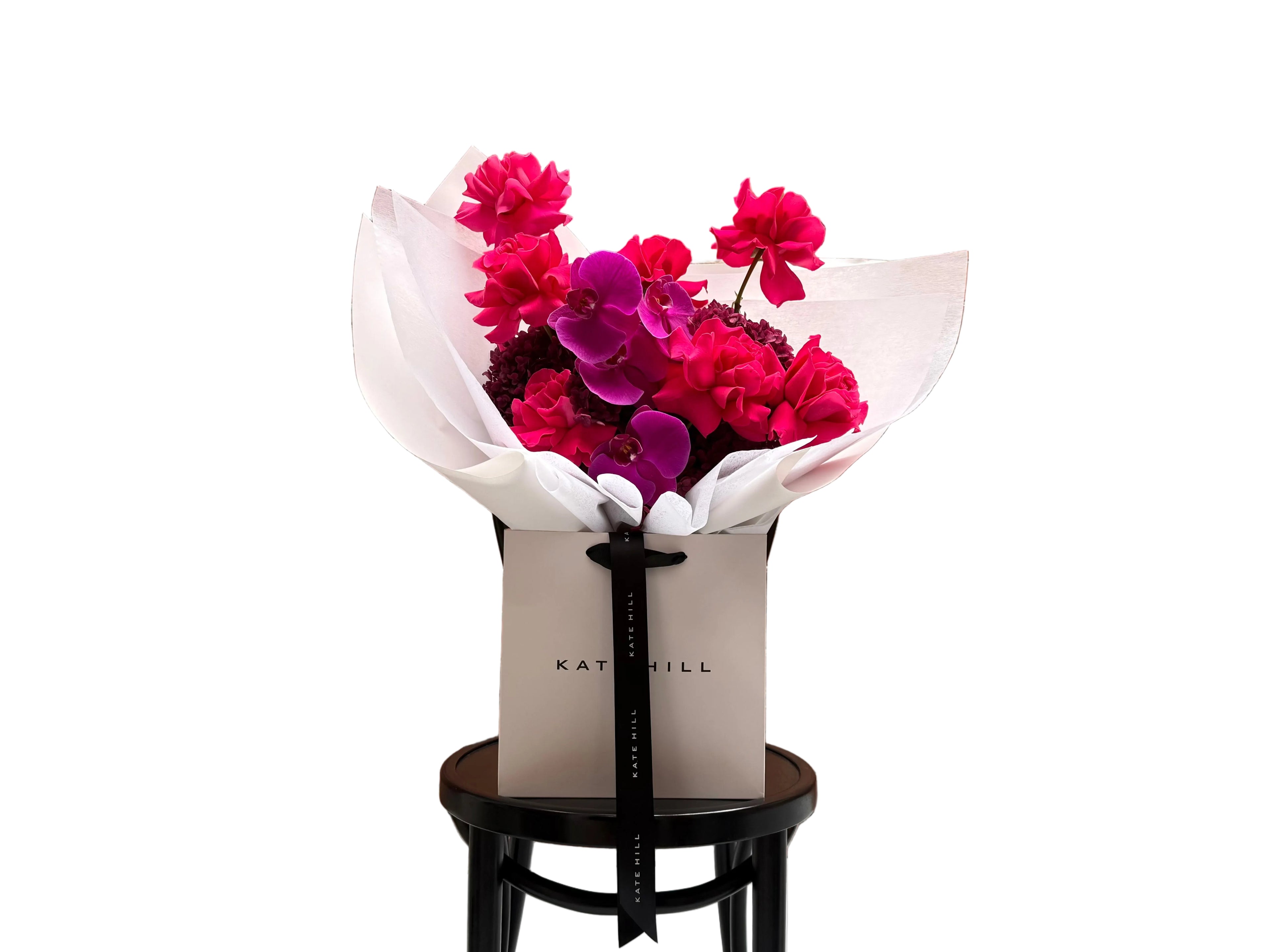 June signature flower bouquet featuring bright pink tones on black chair.
