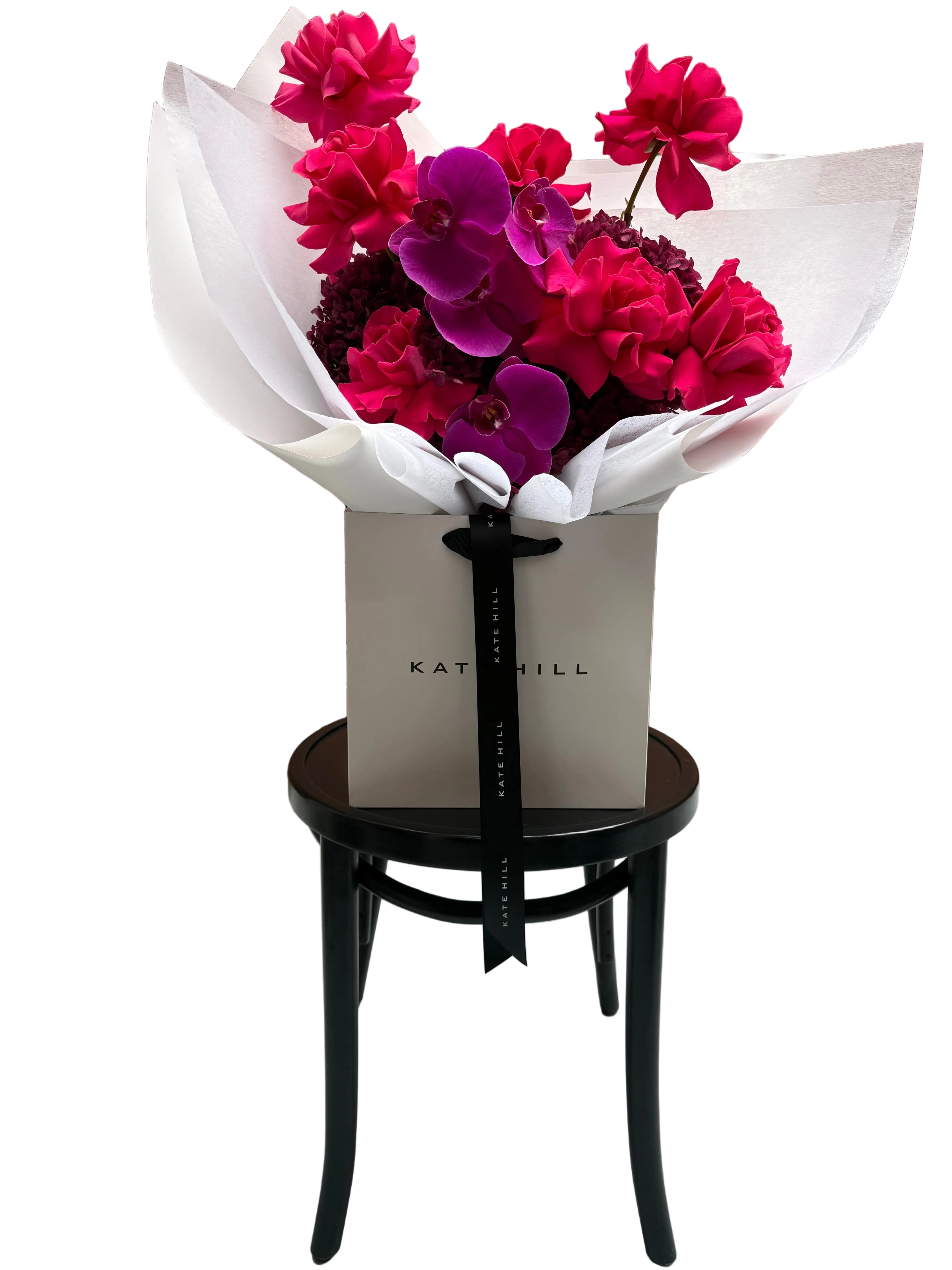 June signature flower bouquet featuring bright pink tones on black chair.