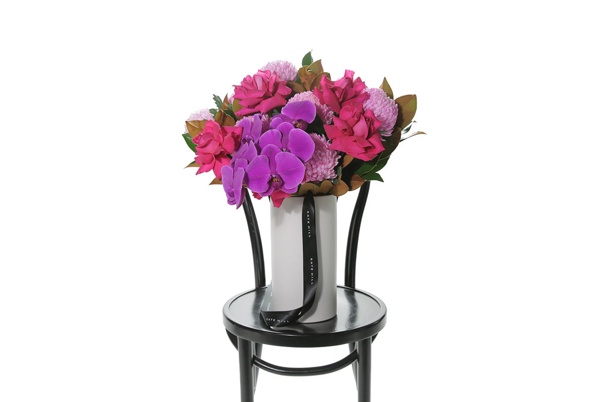 Kate Hill Flowers – large hot-pink birthday vase with roses, disbuds, orchids and magnolia in a white ceramic cylinder.