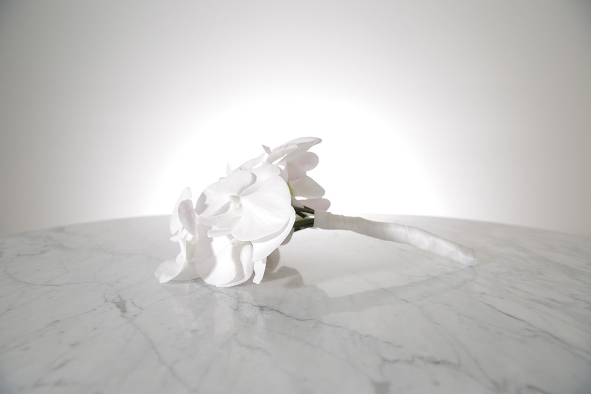 Petite white phalaenopsis orchid bridesmaid bouquet with satin ribbon and pearl pin finish on a marble surface