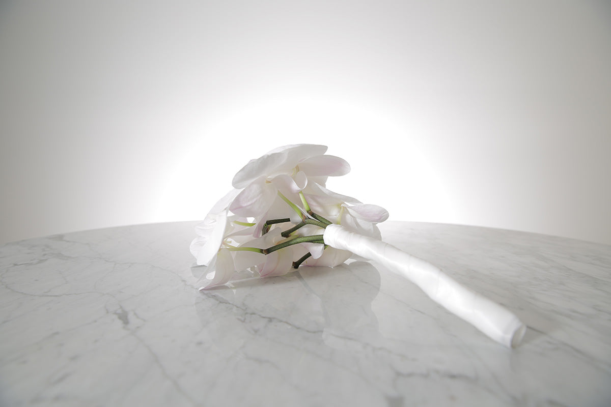 Petite white phalaenopsis orchid bridesmaid bouquet with satin ribbon and pearl pin finish on a marble surface