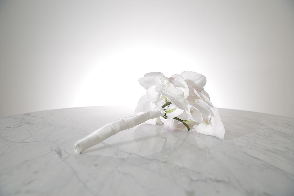 Petite white phalaenopsis orchid bridesmaid bouquet with satin ribbon and pearl pin finish on a marble surface