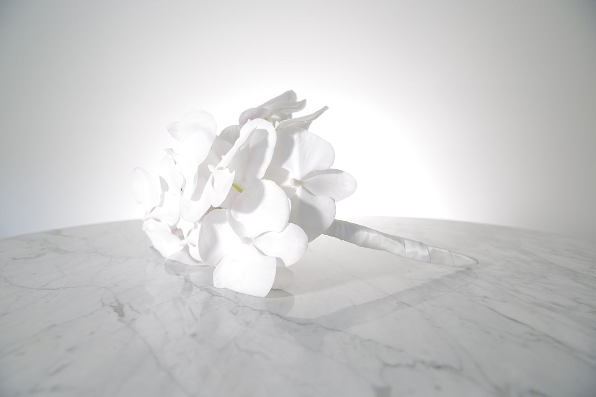 Large cascading white phalaenopsis orchid bridal bouquet bound in satin ribbon on a marble surface with a white background