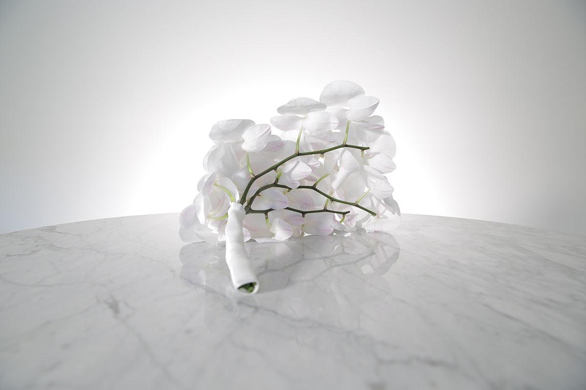 Large cascading white phalaenopsis orchid bridal bouquet bound in satin ribbon on a marble surface with a white background