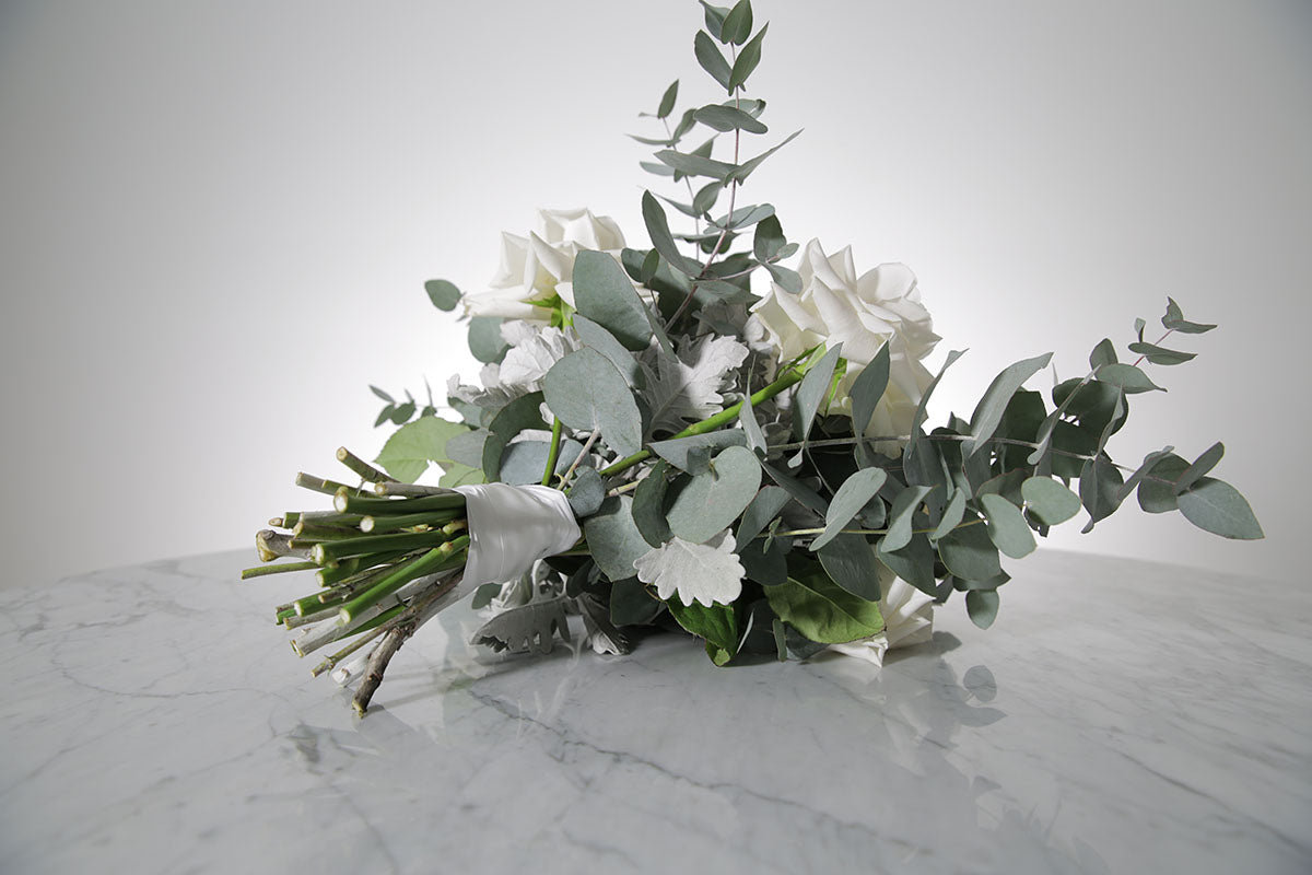 Bridal bouquet of white roses and eucalyptus on a marble surface with a light grey background