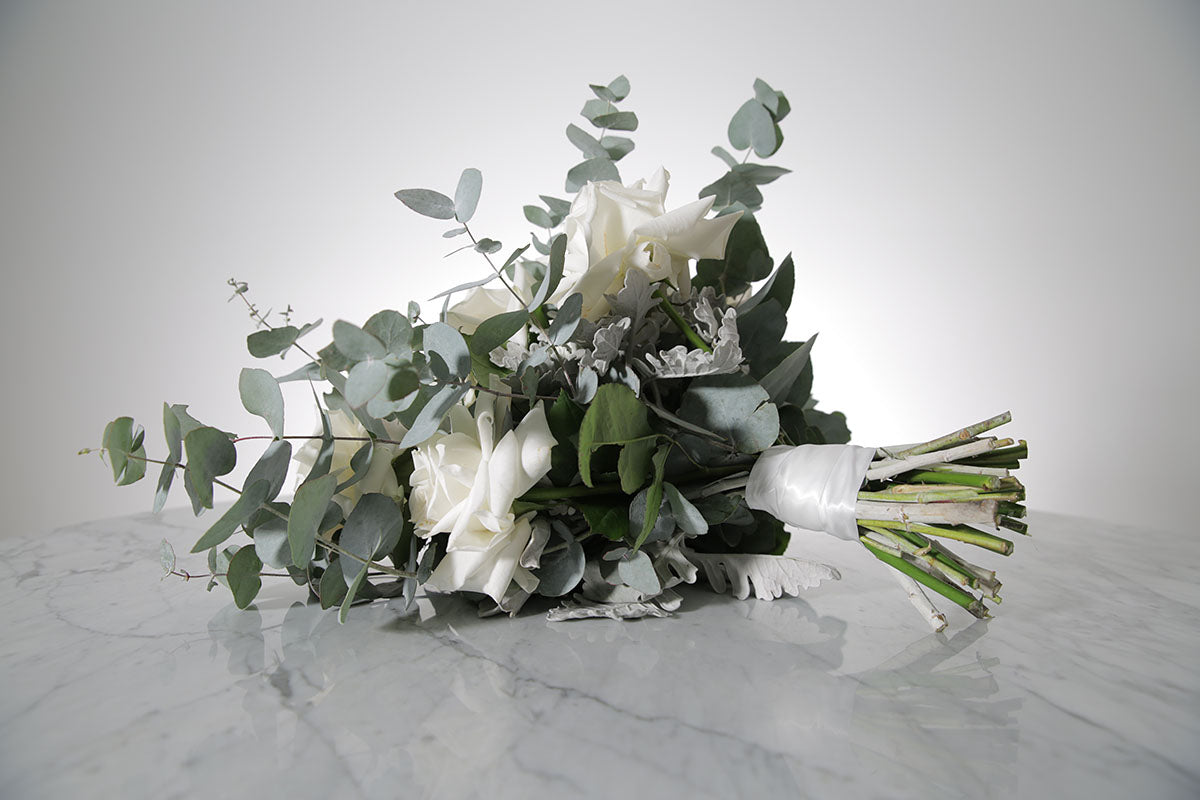 Bridal bouquet of white roses and eucalyptus on a marble surface with a light grey background