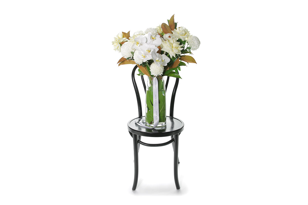 Kate Hill Flowers – large tapered vase with white and lemon roses, chrysanthemums, orchids and monstera lining.