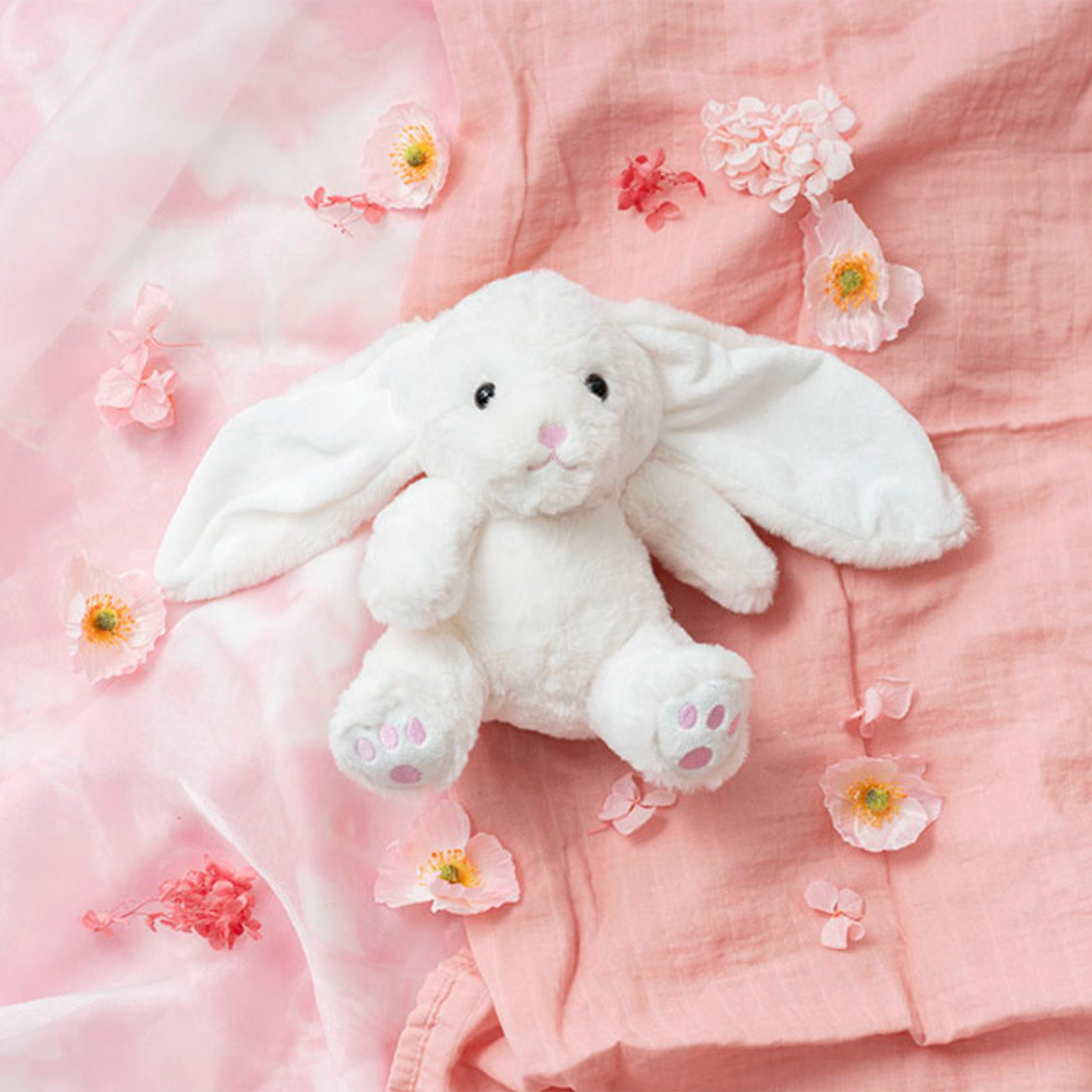 White plush bunny toy on a pink fabric background with flowers