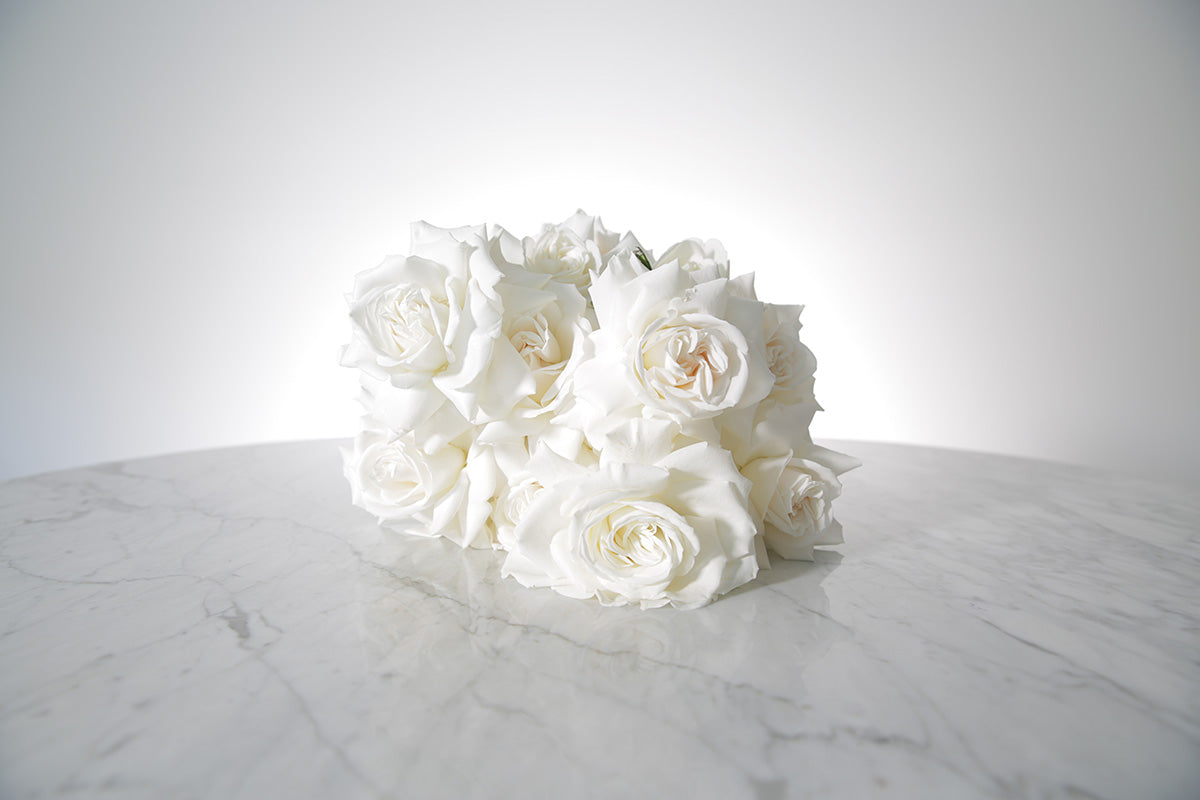 Reflexed white rose bridal bouquet with satin wrap and pearl pin finish placed on marble