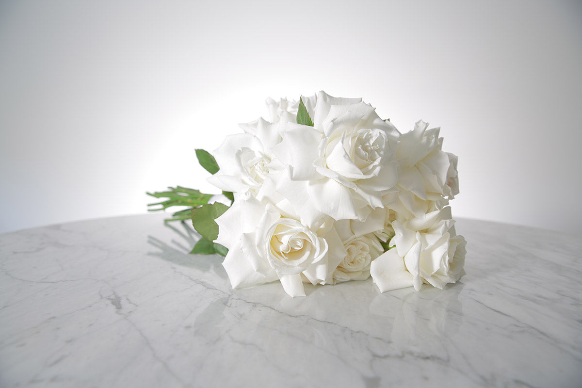 Reflexed white rose bridal bouquet with satin wrap and pearl pin finish placed on marble