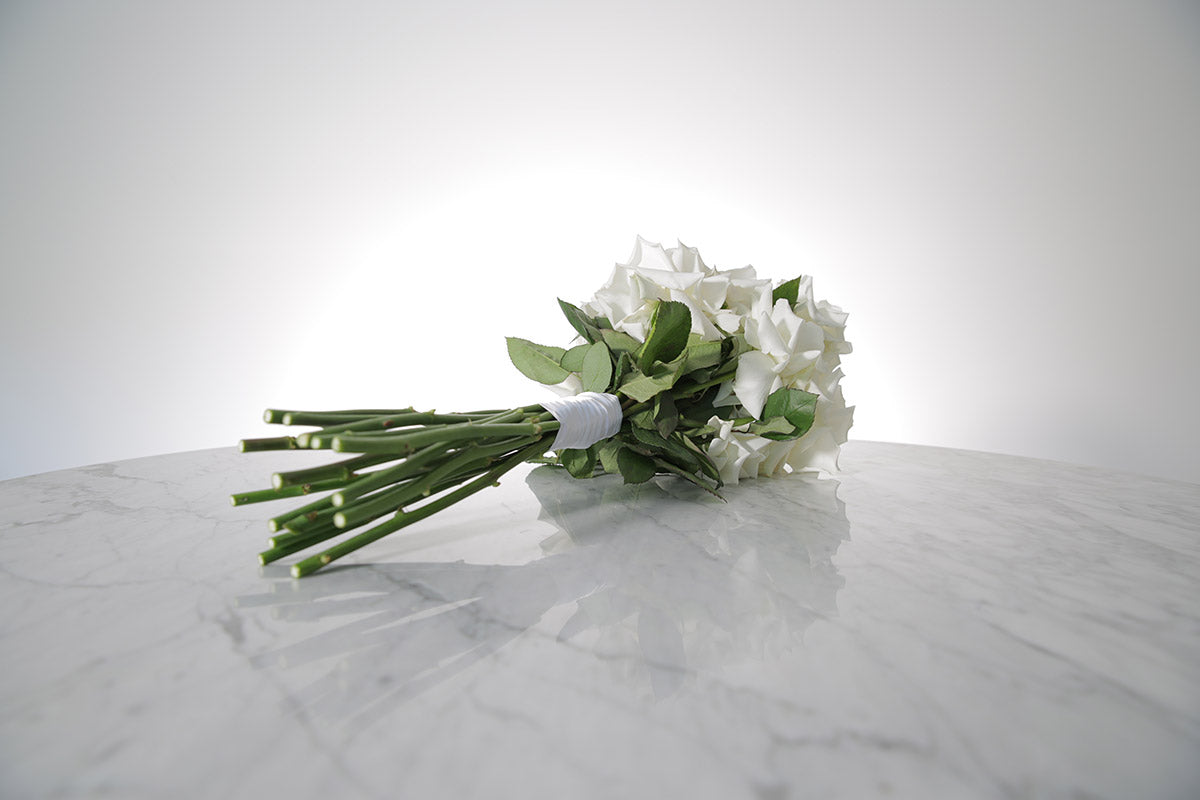 Reflexed white rose bridal bouquet with satin wrap and pearl pin finish placed on marble