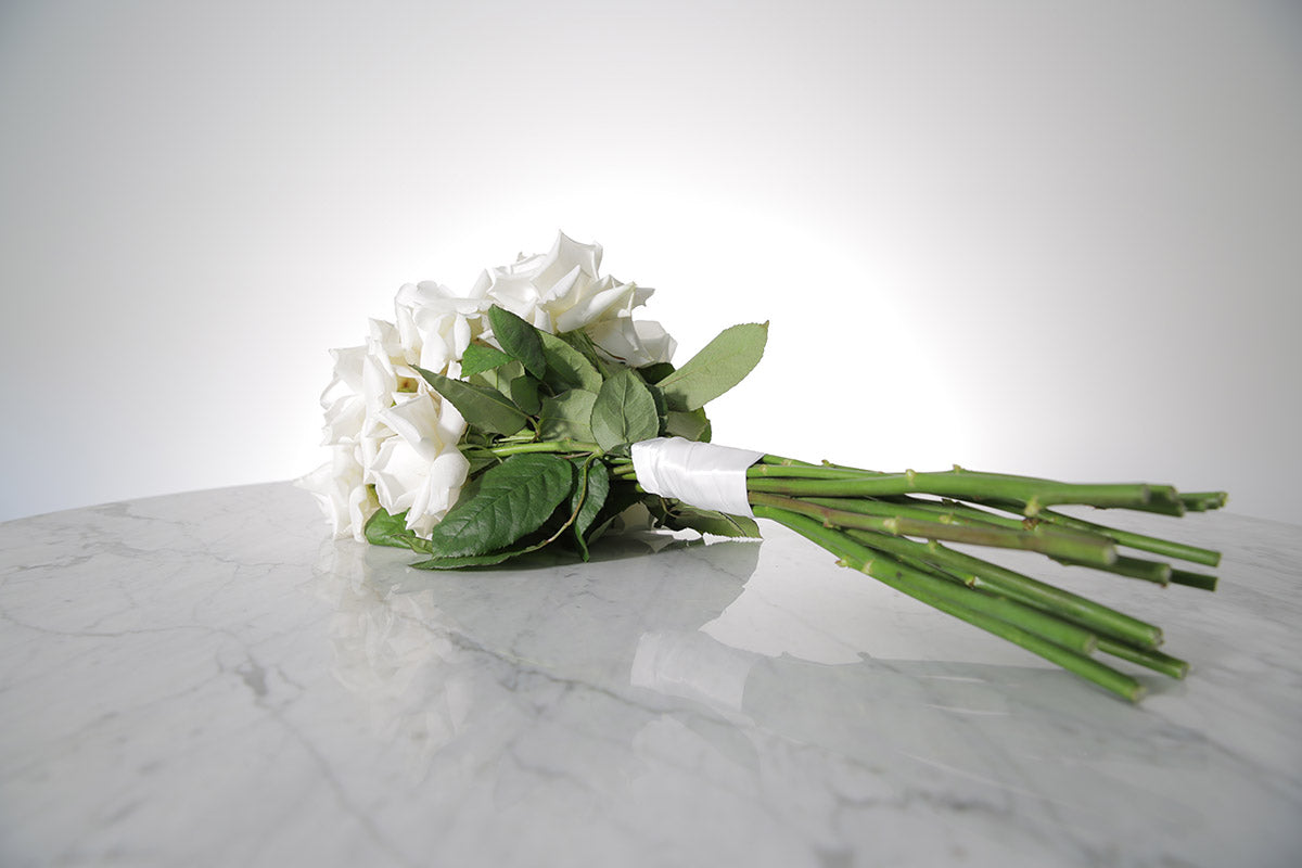 Reflexed white rose bridal bouquet with satin wrap and pearl pin finish placed on marble