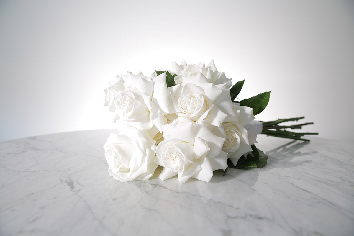 Reflexed white rose bridal bouquet with satin wrap and pearl pin finish placed on marble