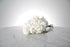 Reflexed white rose bridesmaid bouquet finished with ivory satin ribbon and pearl pin on a marble surface with a light grey background