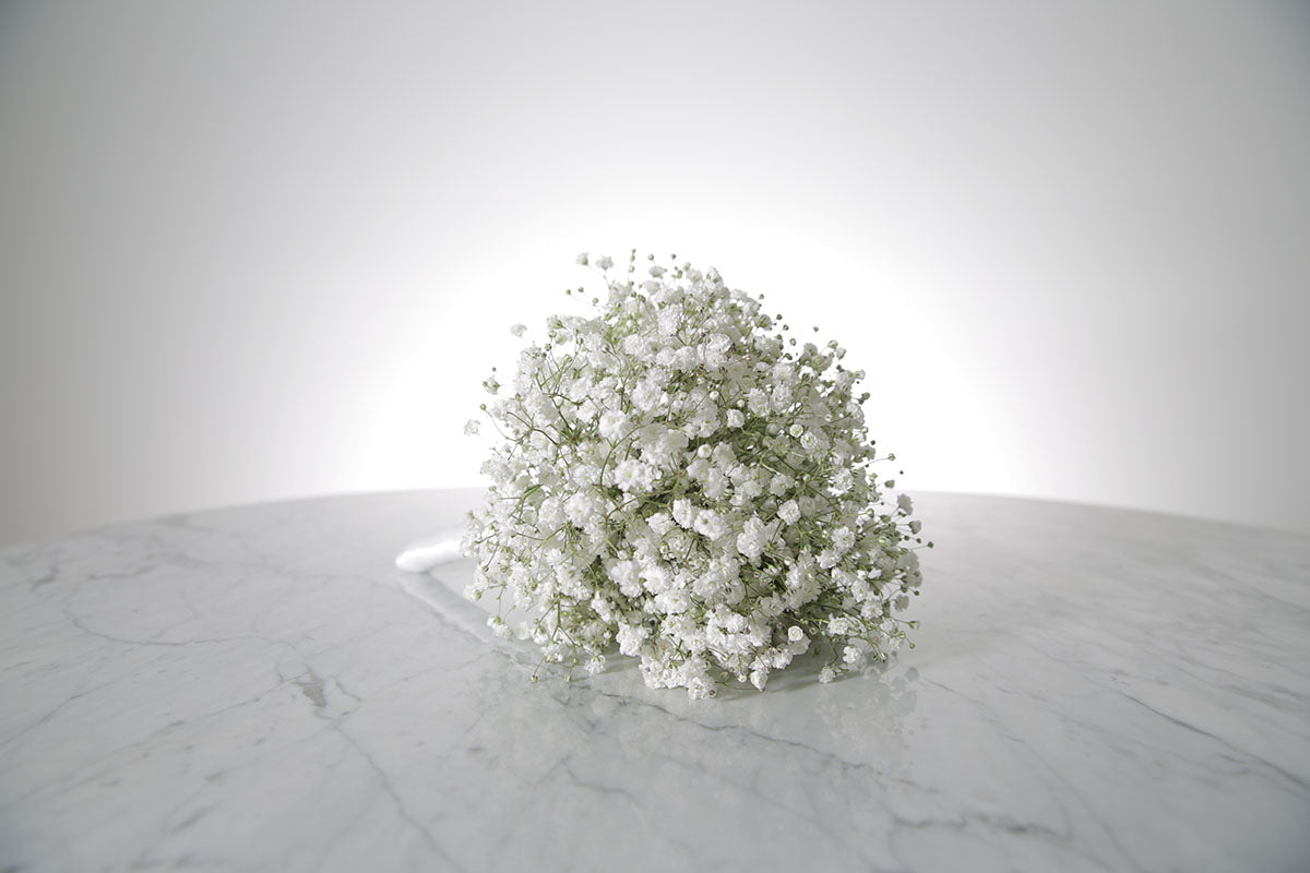 Petite white gypsophila bridesmaid bouquet with satin ribbon and pearl-pin finish placed on a marble surface