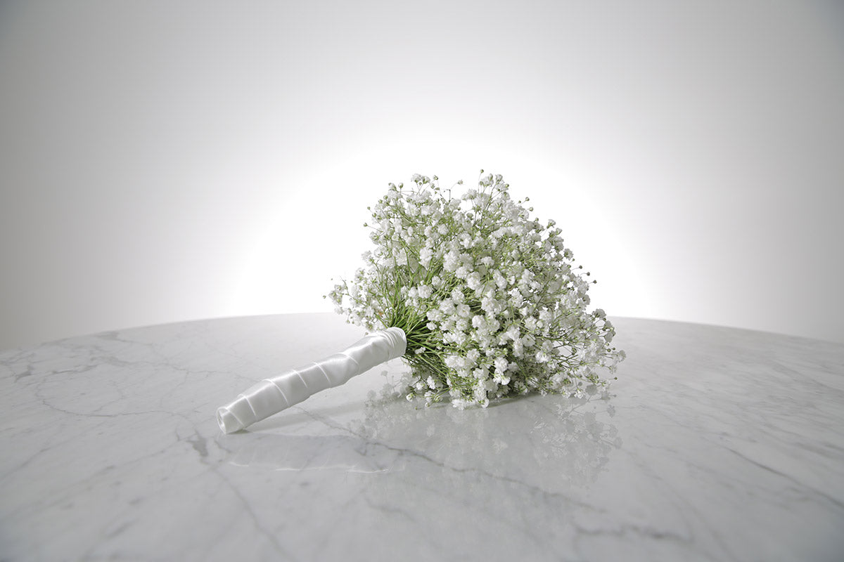 Petite white gypsophila bridesmaid bouquet with satin ribbon and pearl-pin finish placed on a marble surface