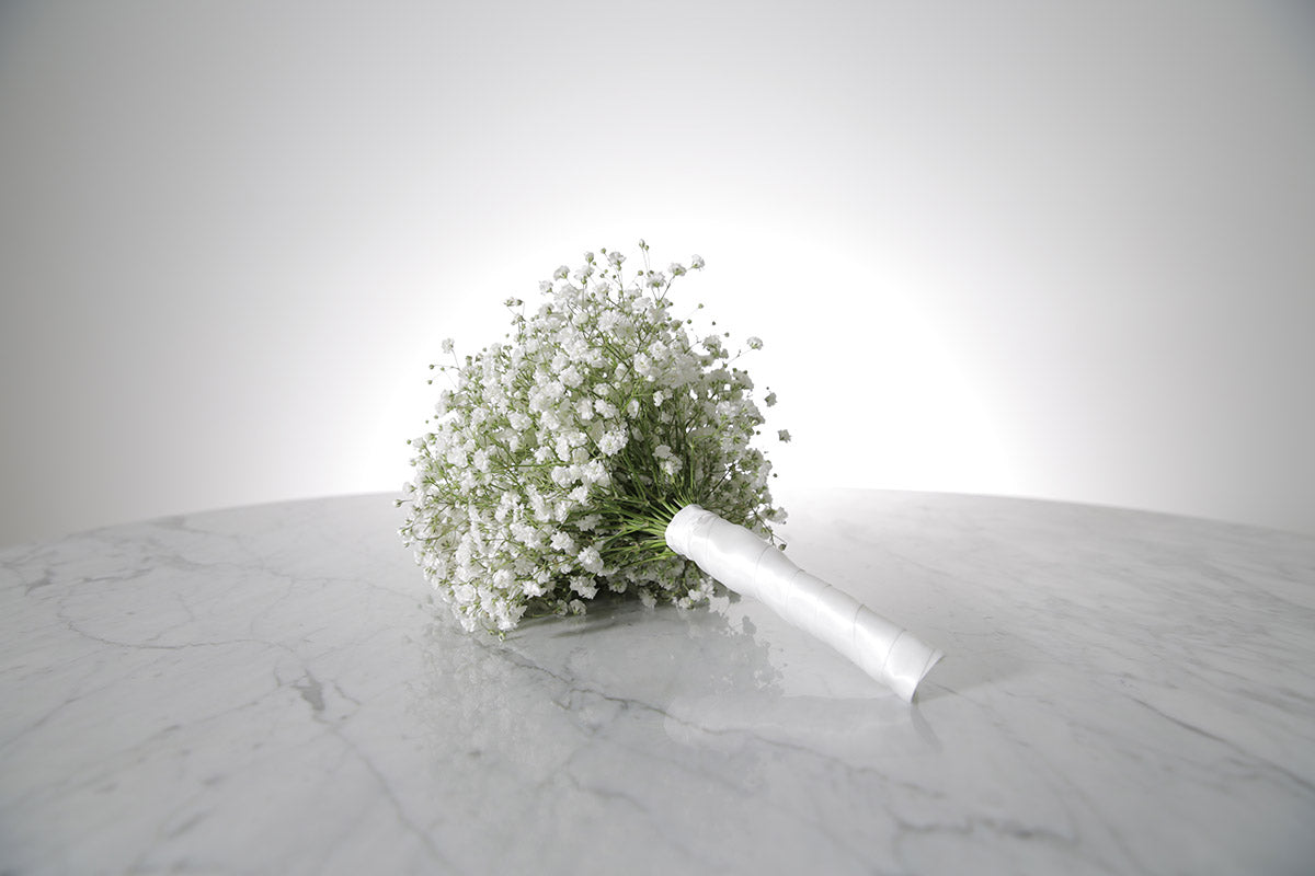 Petite white gypsophila bridesmaid bouquet with satin ribbon and pearl-pin finish placed on a marble surface