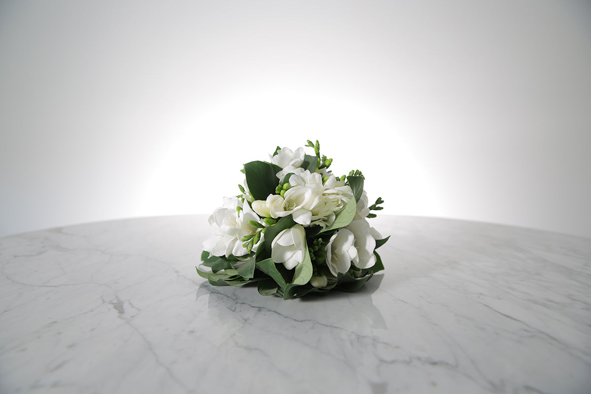 Petite bridesmaid bouquet of white freesias bound in ivory satin on a marble surface