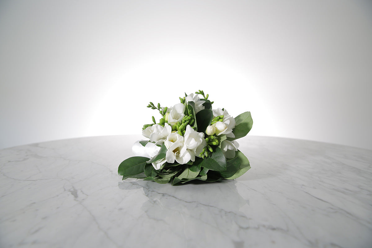 Petite bridesmaid bouquet of white freesias bound in ivory satin on a marble surface