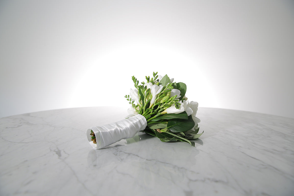 Petite bridesmaid bouquet of white freesias bound in ivory satin on a marble surface