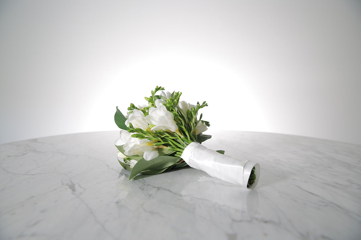 Petite bridesmaid bouquet of white freesias bound in ivory satin on a marble surface