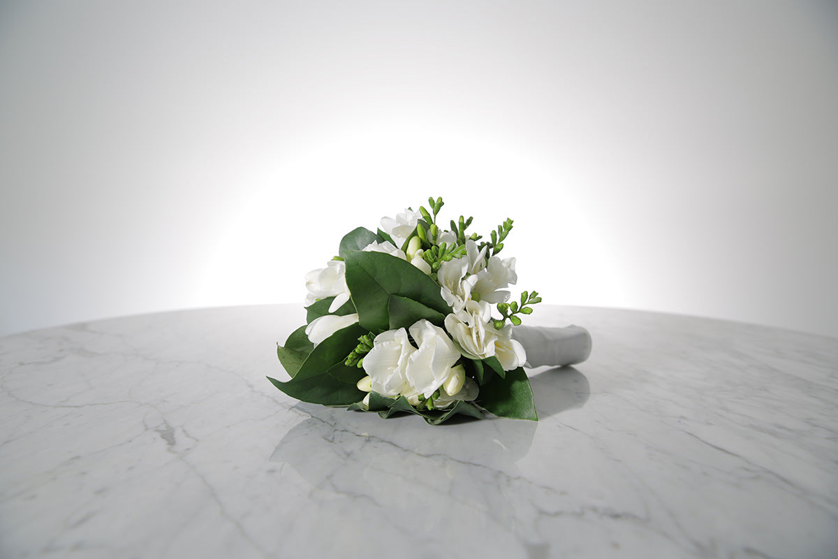 Petite bridesmaid bouquet of white freesias bound in ivory satin on a marble surface
